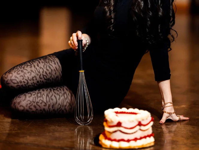 Baker posing with a whisk and cake in a stylish setting