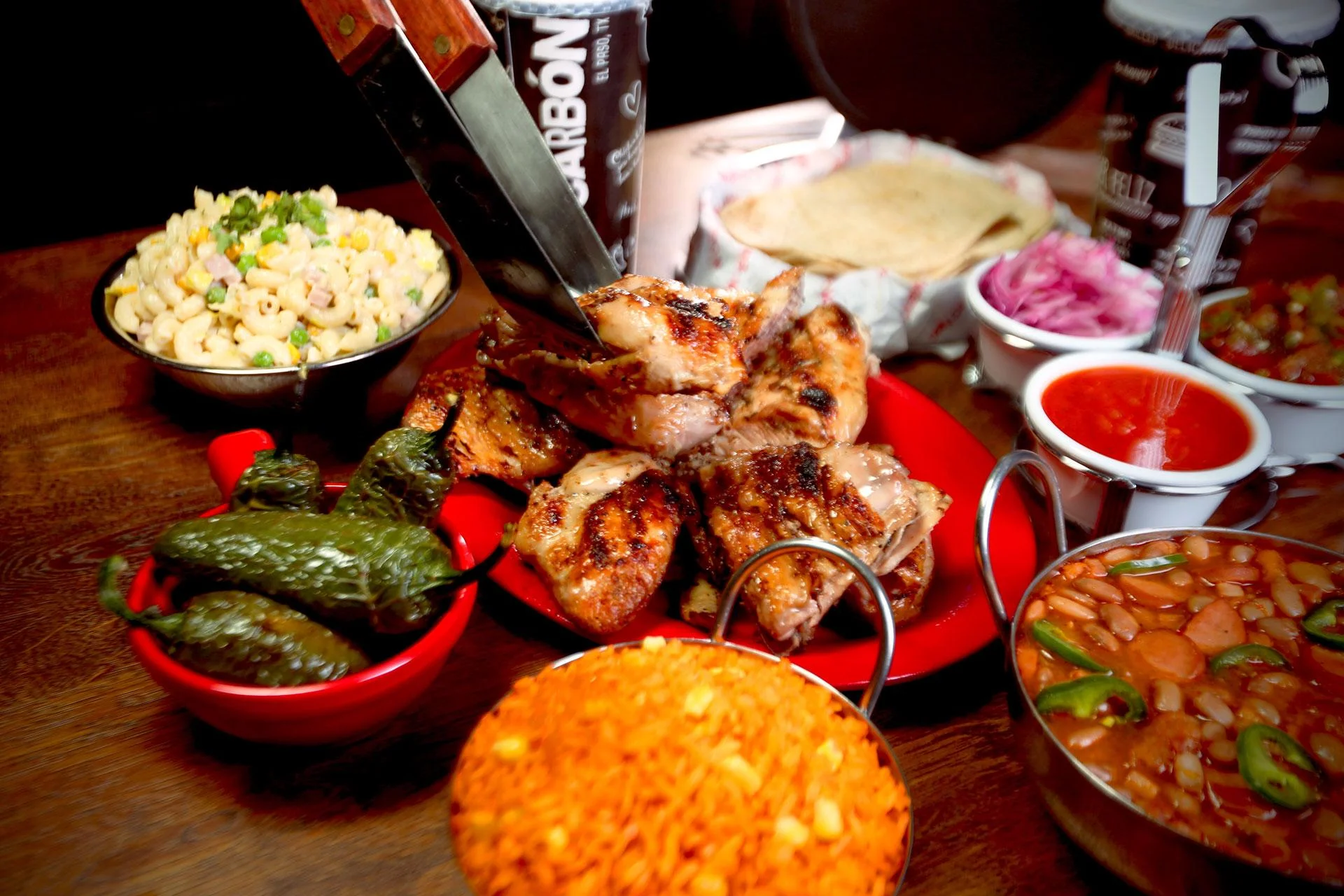 A colorful assortment of grilled chicken, rice, and sides featuring jalapeños, pasta salad, and beans, presented on a vibrant red dish.