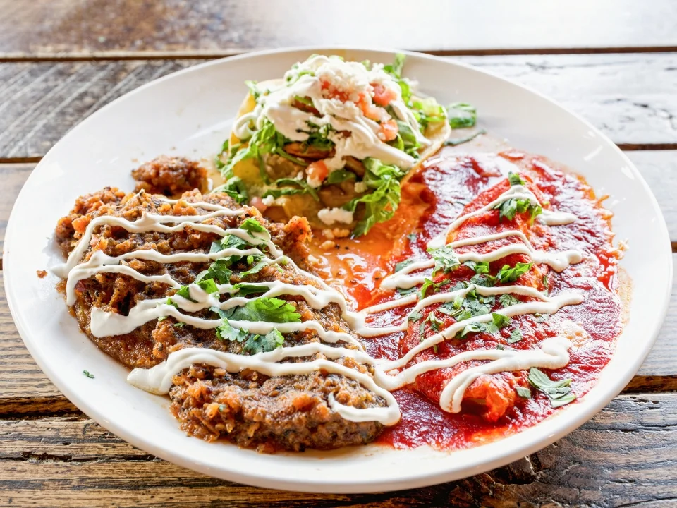 A delicious plate with a variety of Mexican dishes, featuring a serving of enchiladas, a meat dish, and a fresh taco with vegetables and sauce.