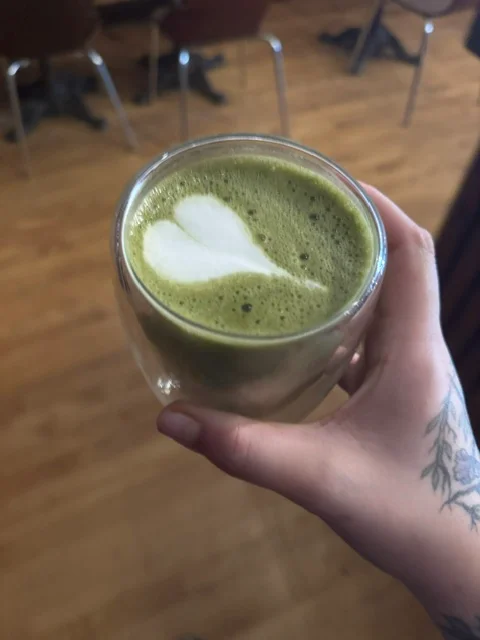 Matcha latte with heart-shaped foam art in a clear glass cup