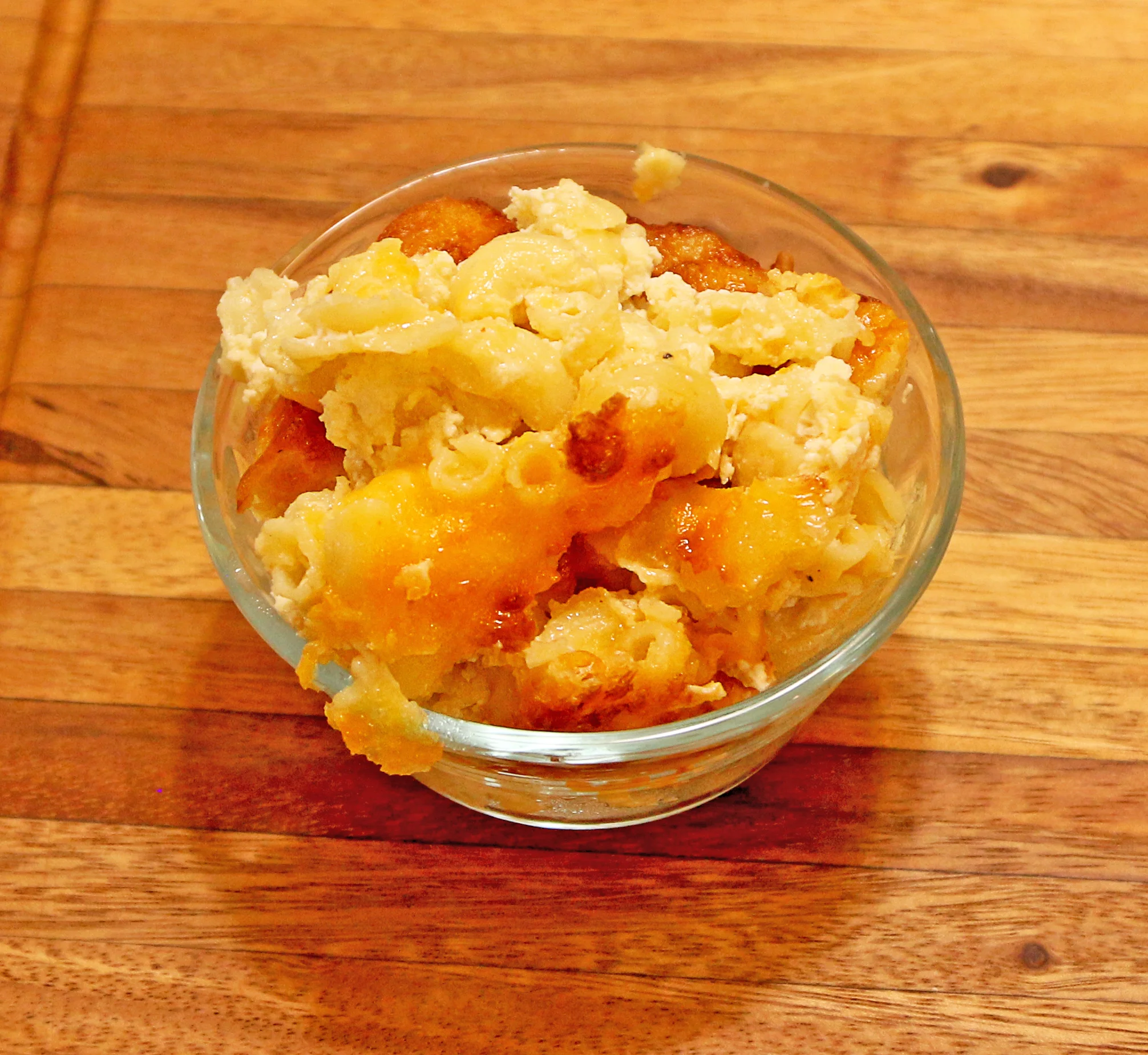 A serving of baked macaroni and cheese in a glass bowl. The dish features creamy pasta topped with a golden, baked cheese layer.