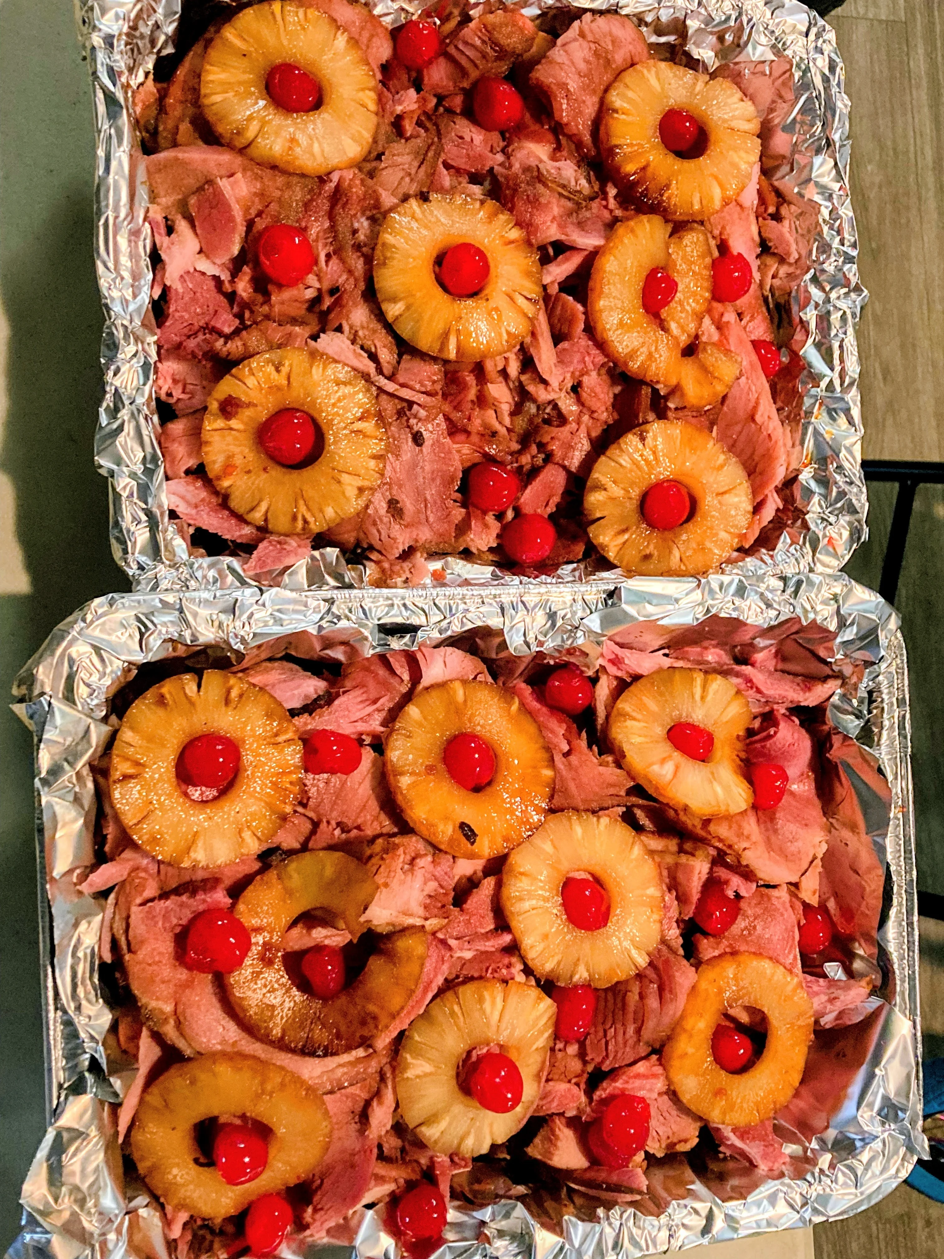 A dish featuring sliced ham, pineapple rings, and maraschino cherries, elegantly arranged in a foil tray.