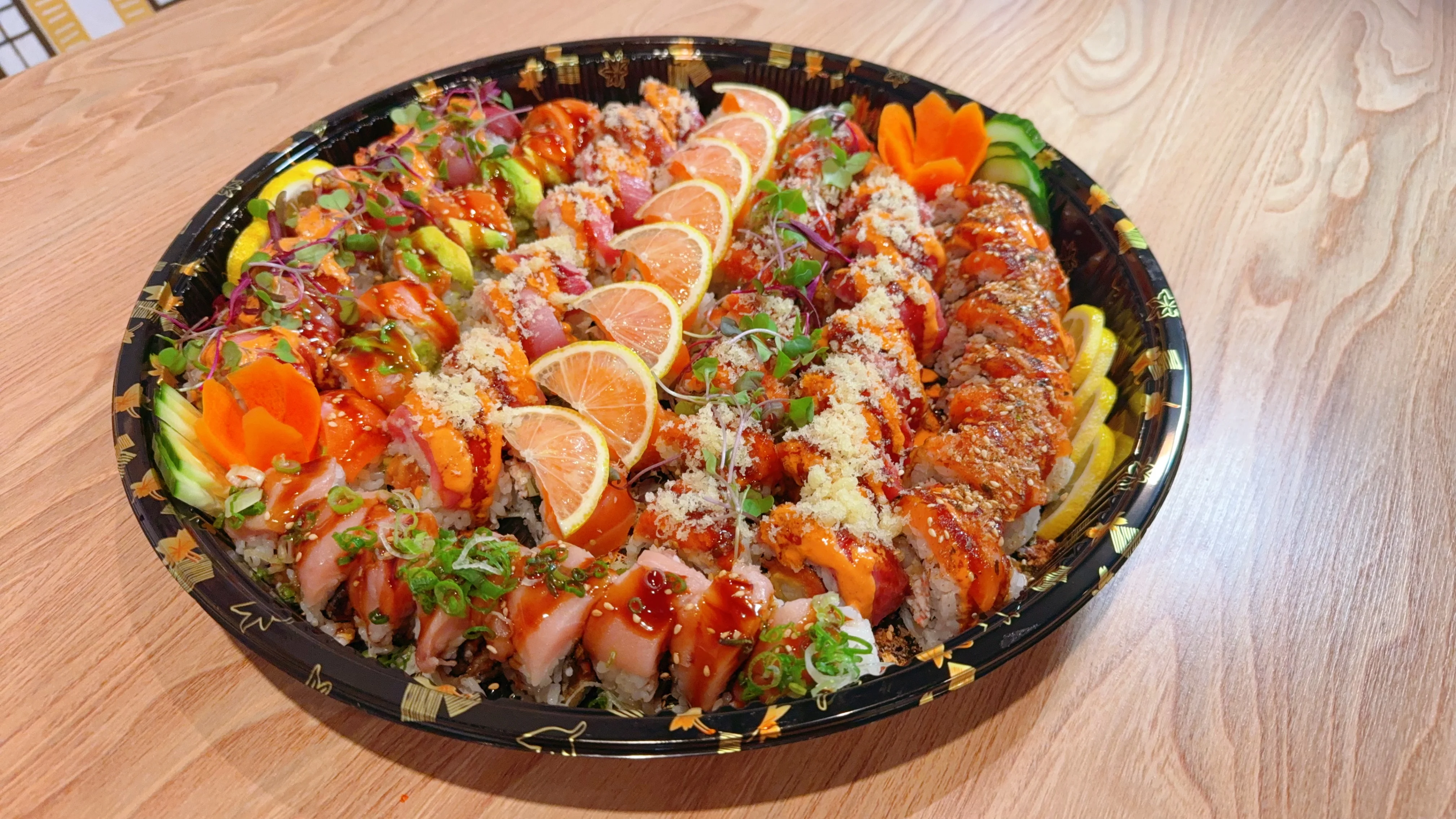 A colorful sushi platter featuring various rolls and sashimi, garnished with green leaves and presented in a circular tray.