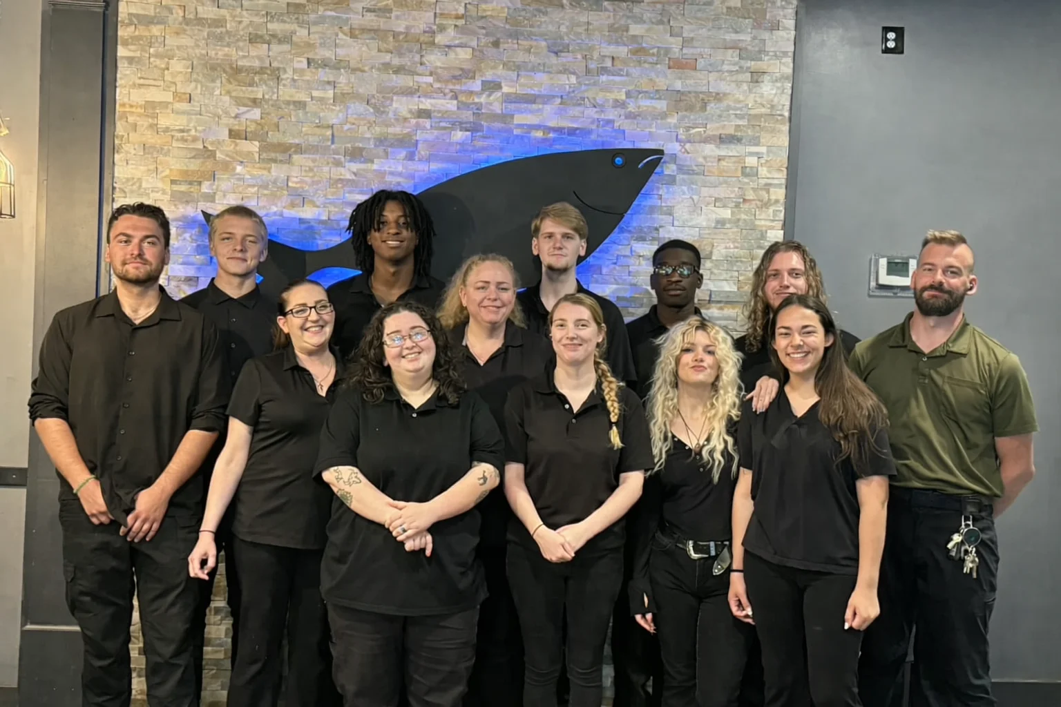 Restaurant staff posing together in front of a decorative wall