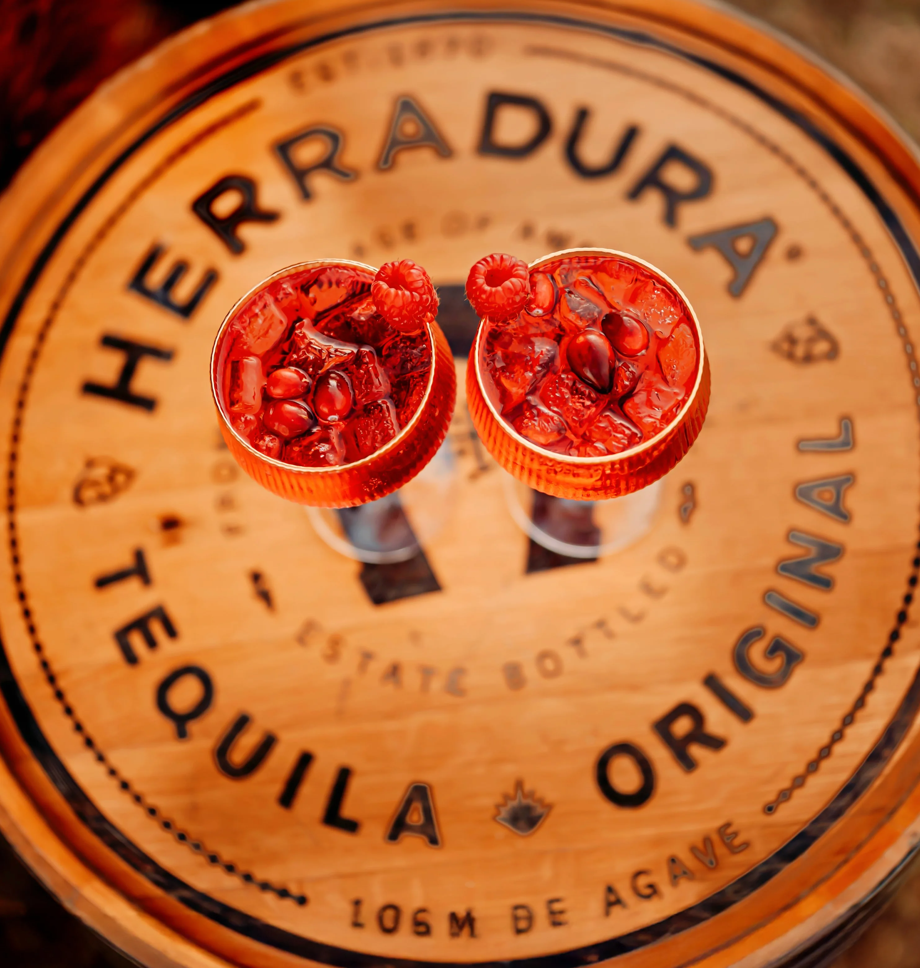 Two vibrant cocktails on a Herradura tequila barrel