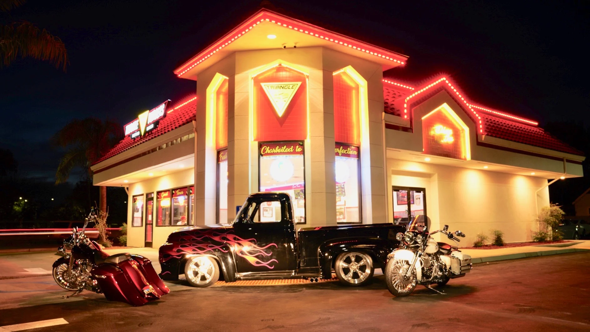 Vibrant diner exterior with classic cars and motorcycles at night