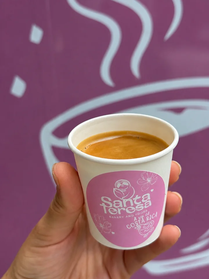 A small cup of espresso with a rich crema, held against a purple background featuring whimsical steam designs.