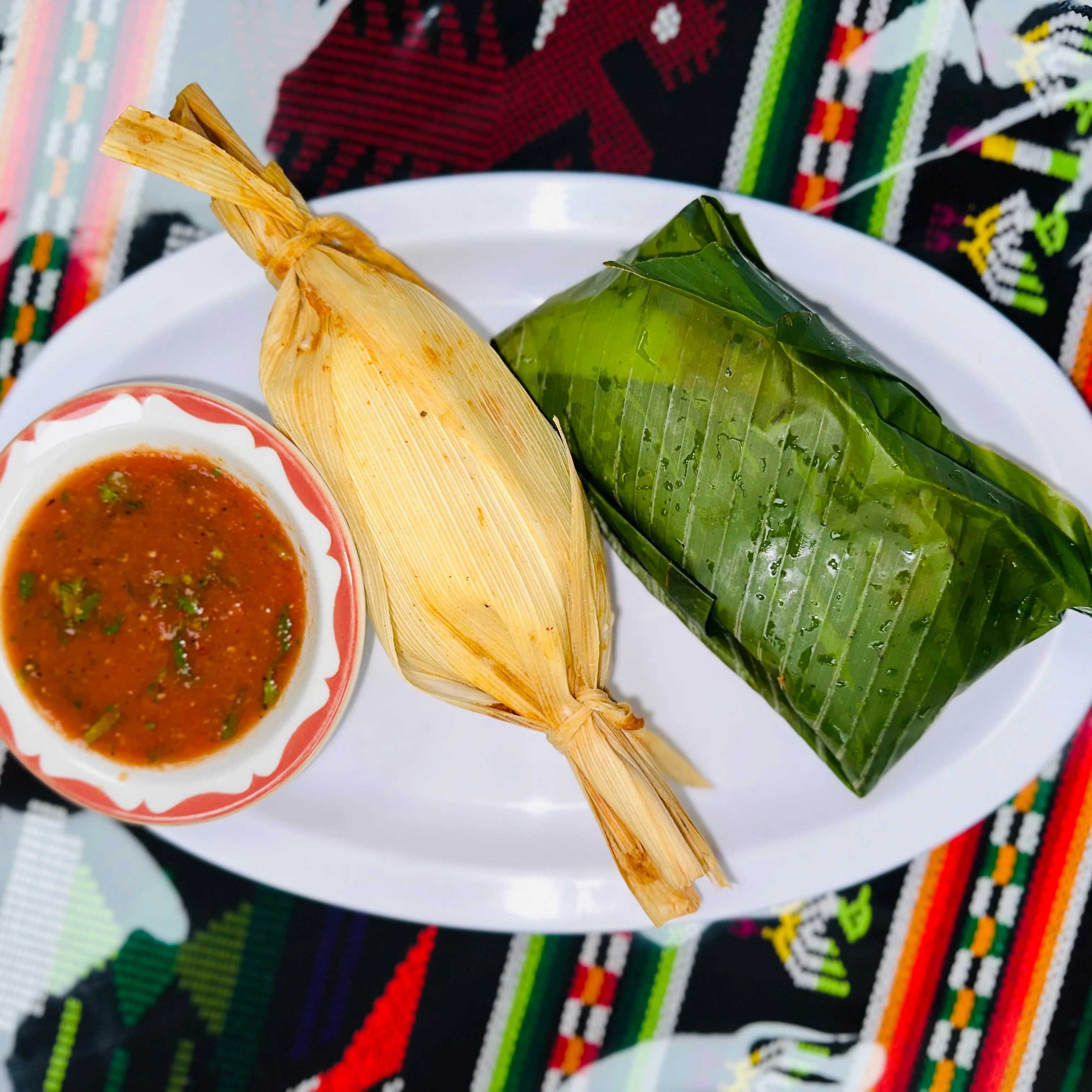 Traditional Mexican tamales with salsa on a colorful tablecloth