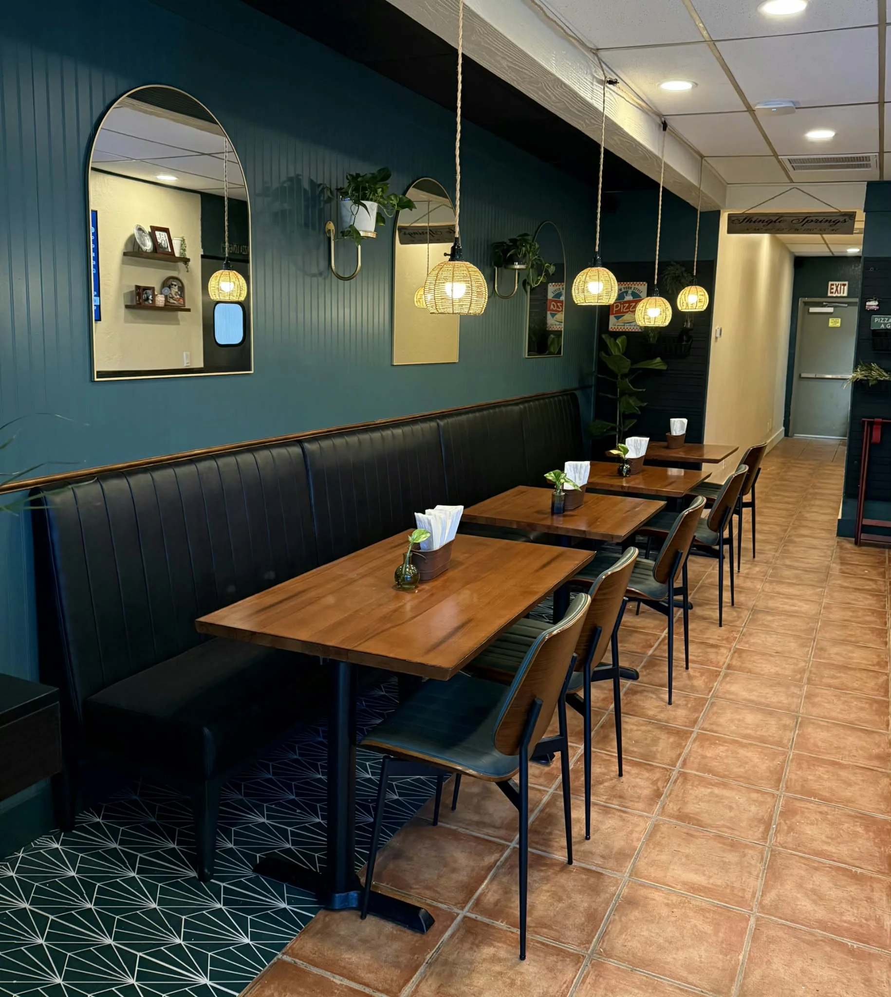 Modern restaurant dining room with booths, wooden tables, mirrors, and pendant lighting