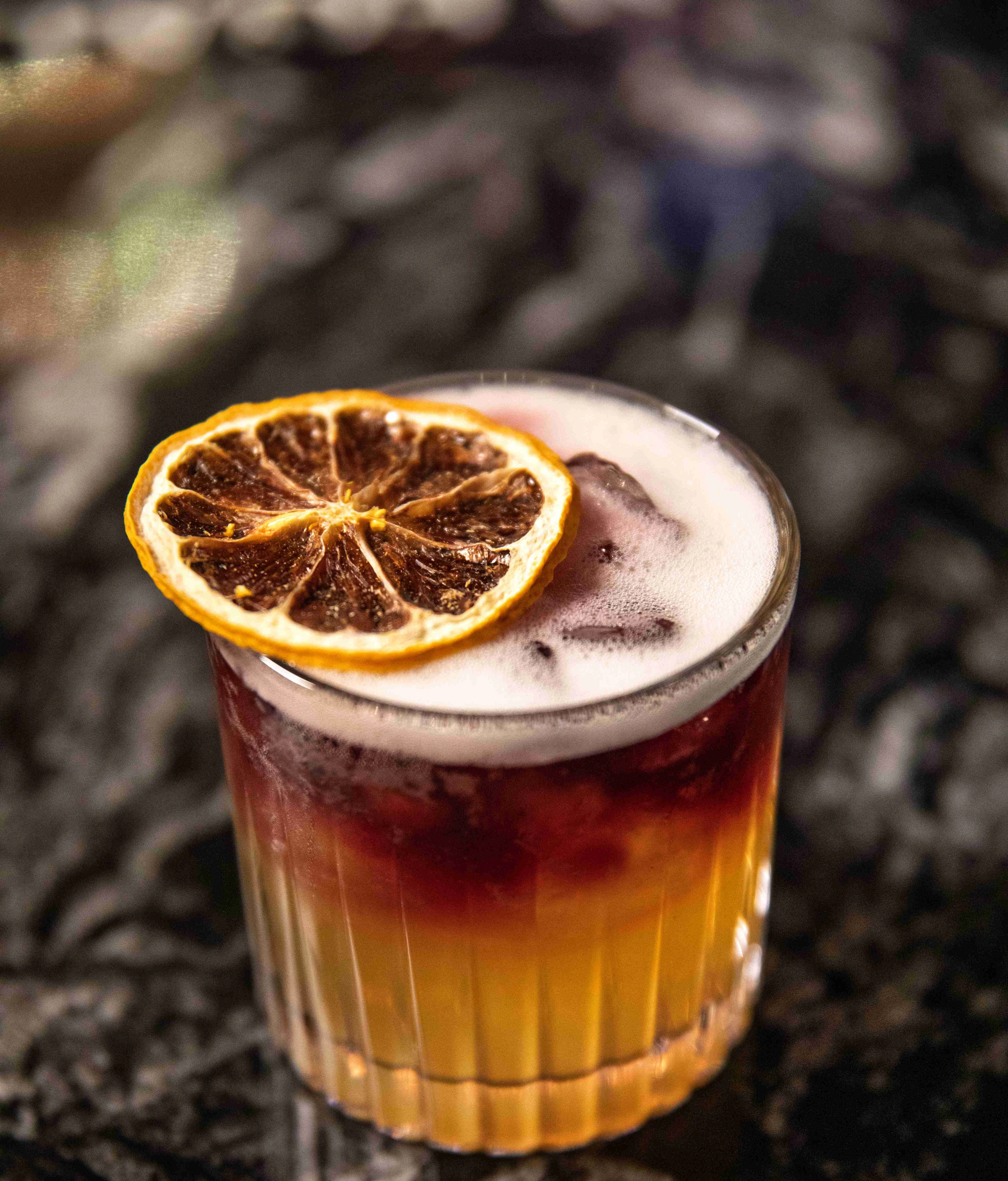 Colorful layered cocktail with dried lemon slice on top