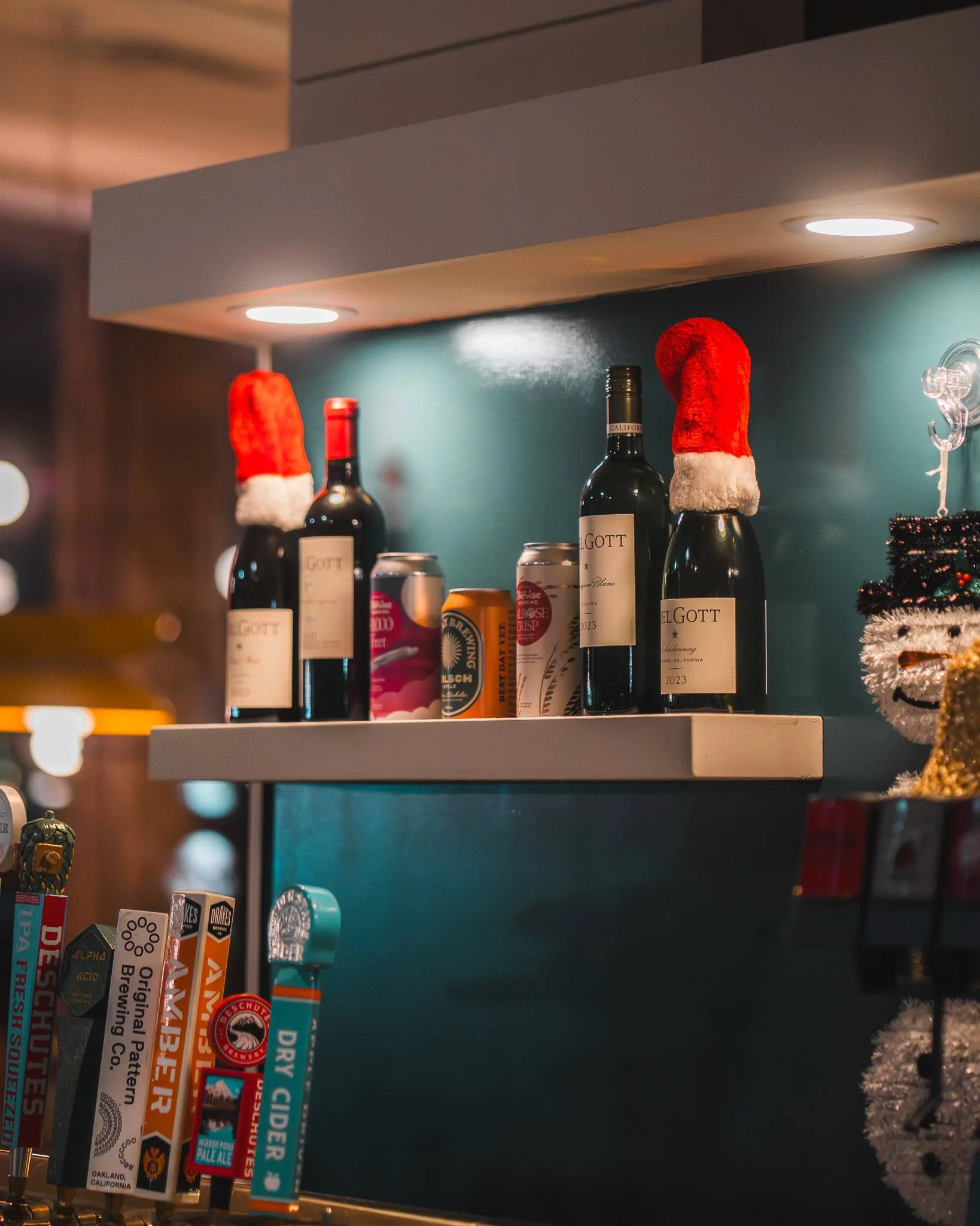 A shelf displaying various bottles of wine and beverages, adorned with festive Santa hats.