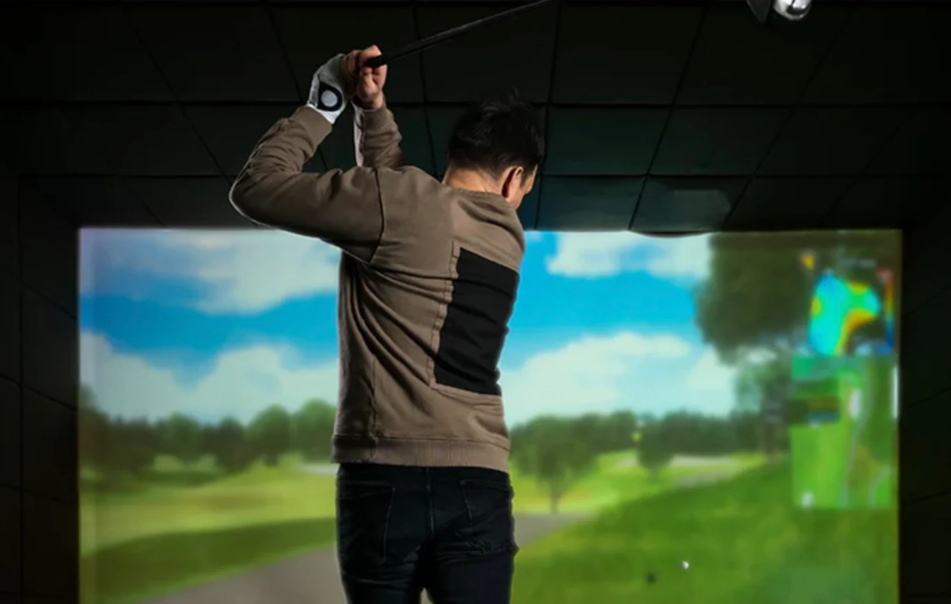 Golfer swinging in a virtual golf simulator with scenic background