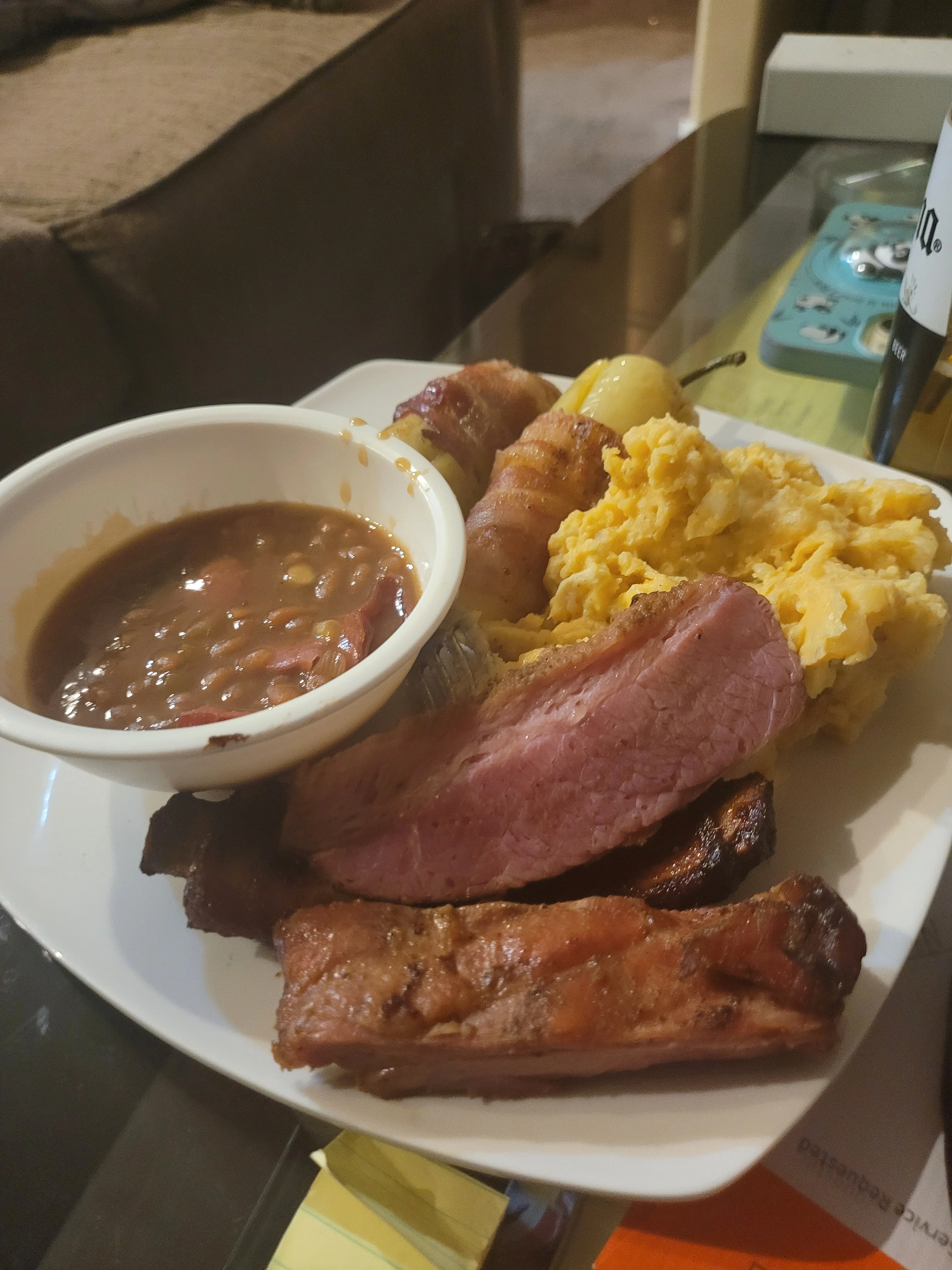 A plate filled with various meats, mashed potatoes, and baked beans. The meal looks hearty and plentiful.