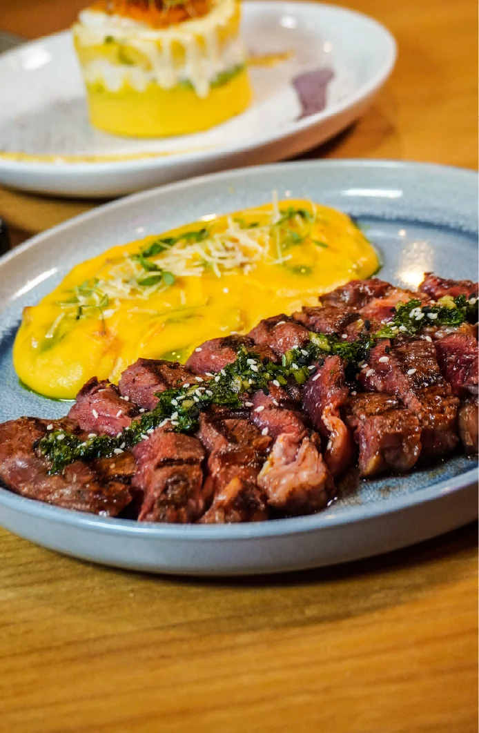 Grilled steak with sauce and creamy yellow side dish on a plate.