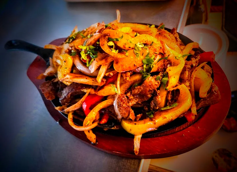 A sizzling plate of fajitas with pieces of marinated beef, bell peppers, and onions, garnished with fresh cilantro.