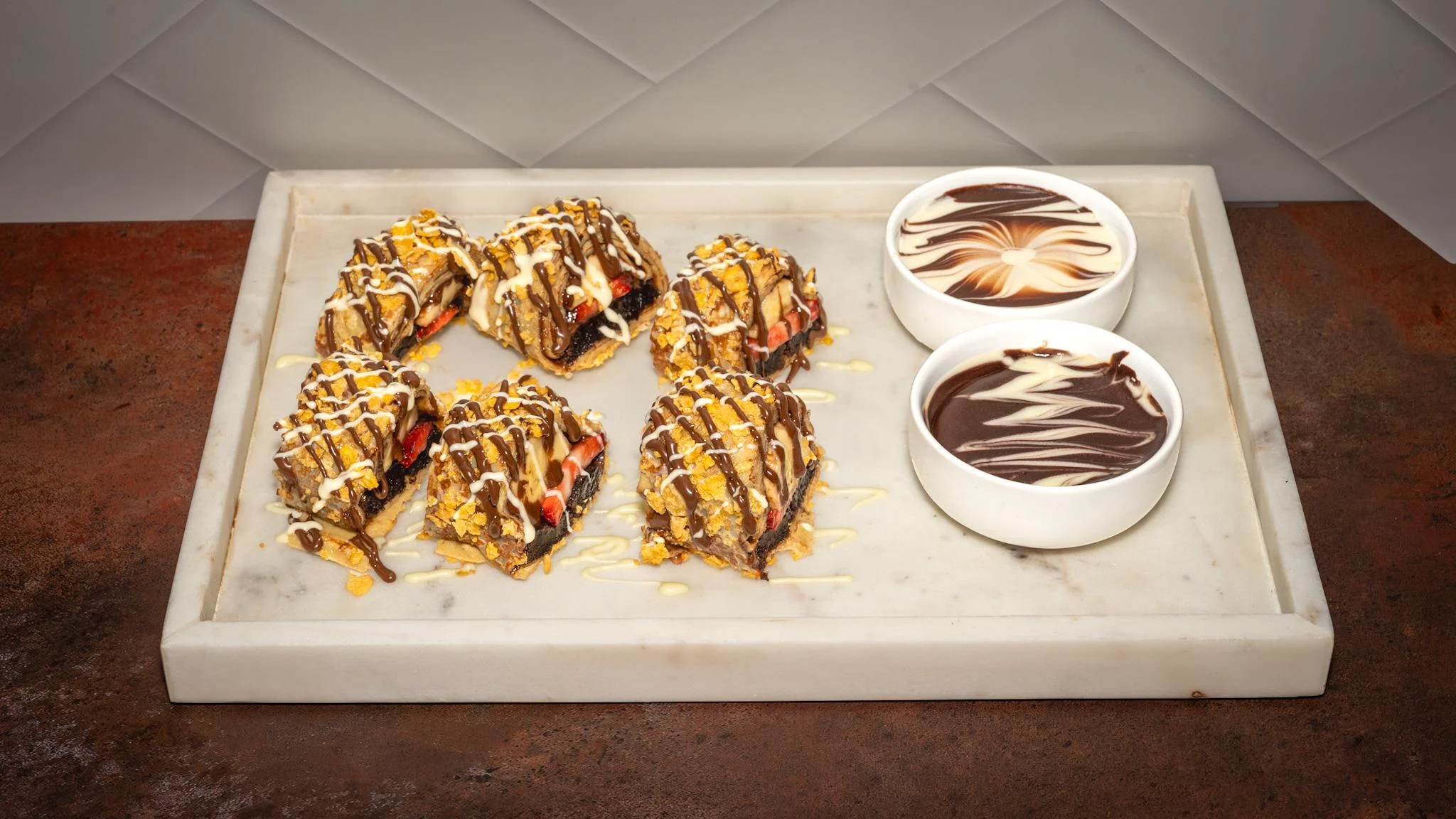 A plate of bite-sized treats drizzled with chocolate and accompanied by two bowls of chocolate sauce for dipping.