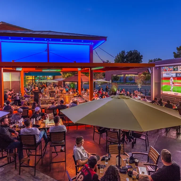 Outdoor dining area with vibrant lighting and a large screen for sports viewing