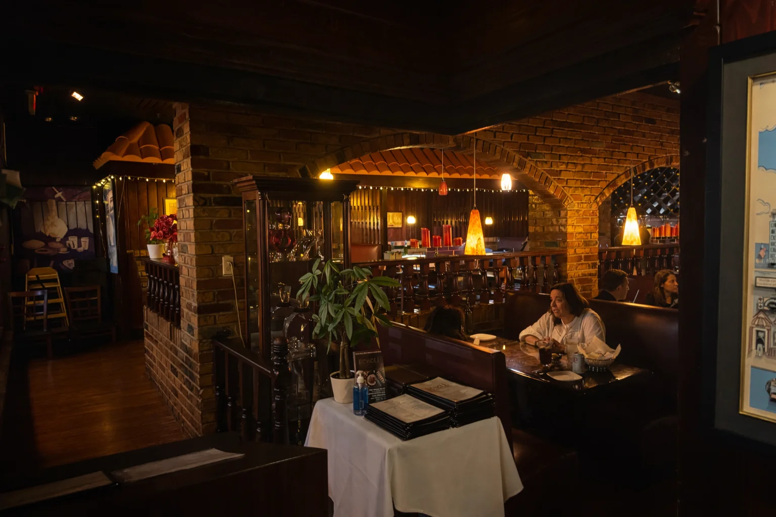 A cozy restaurant interior featuring wooden furnishings, warm lighting, and potted plants. Patrons are seated at booths and tables, enjoying their meals.