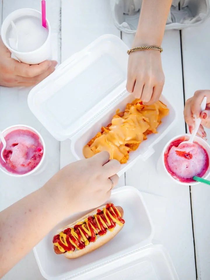 A hand holding a hot dog generously topped with yellow mustard and red ketchup.