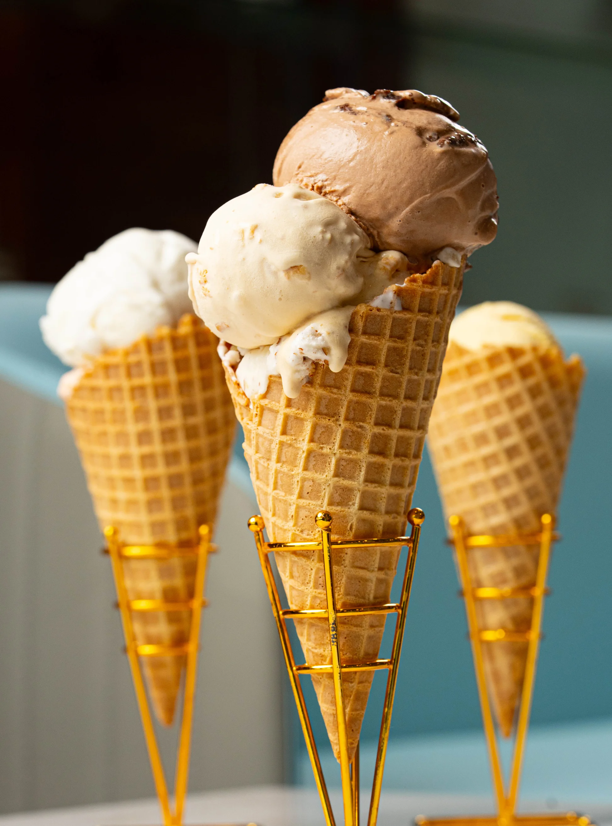 Three ice cream cones with different flavors in golden holders.