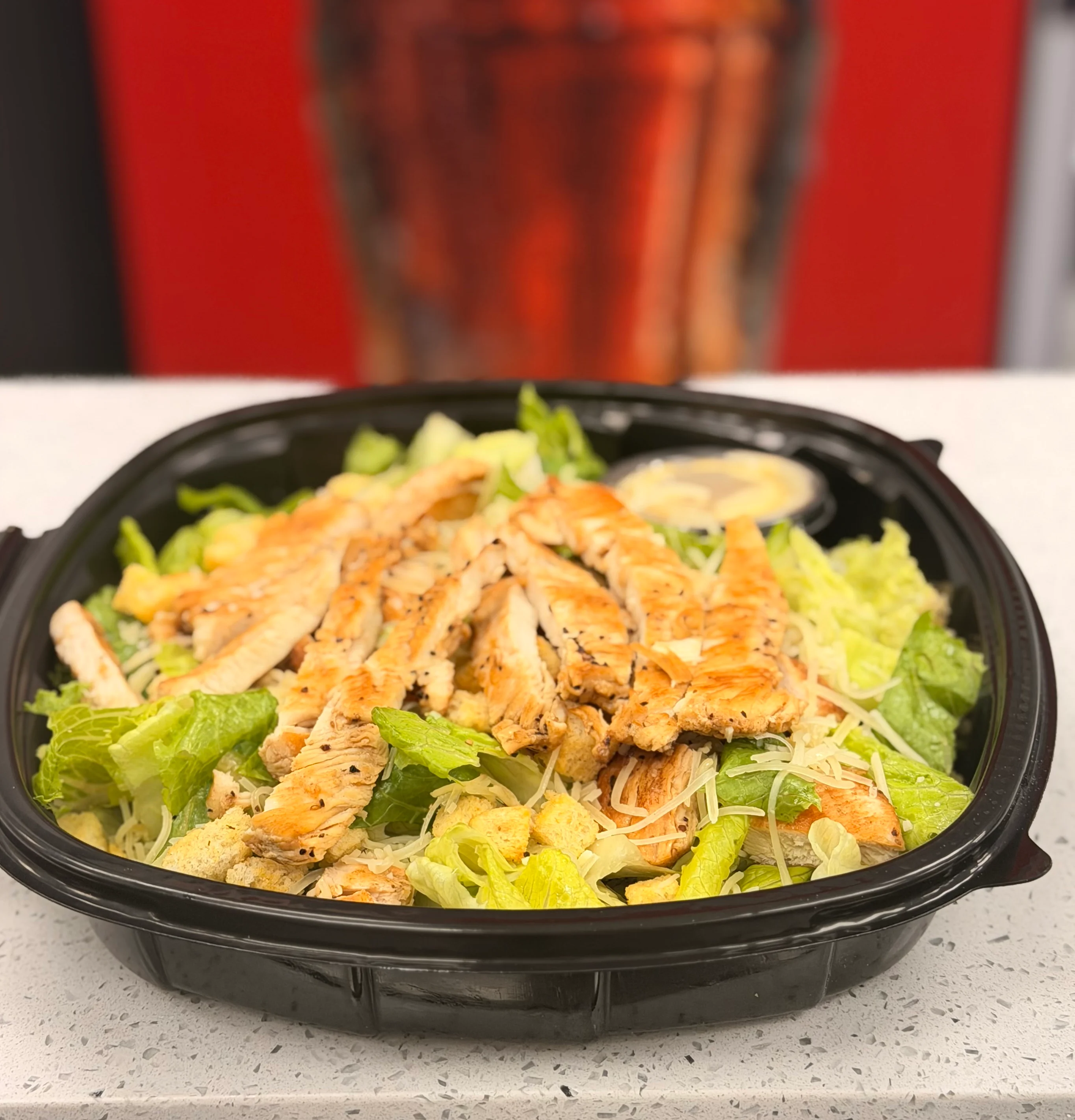 Grilled chicken Caesar salad in a black takeout container