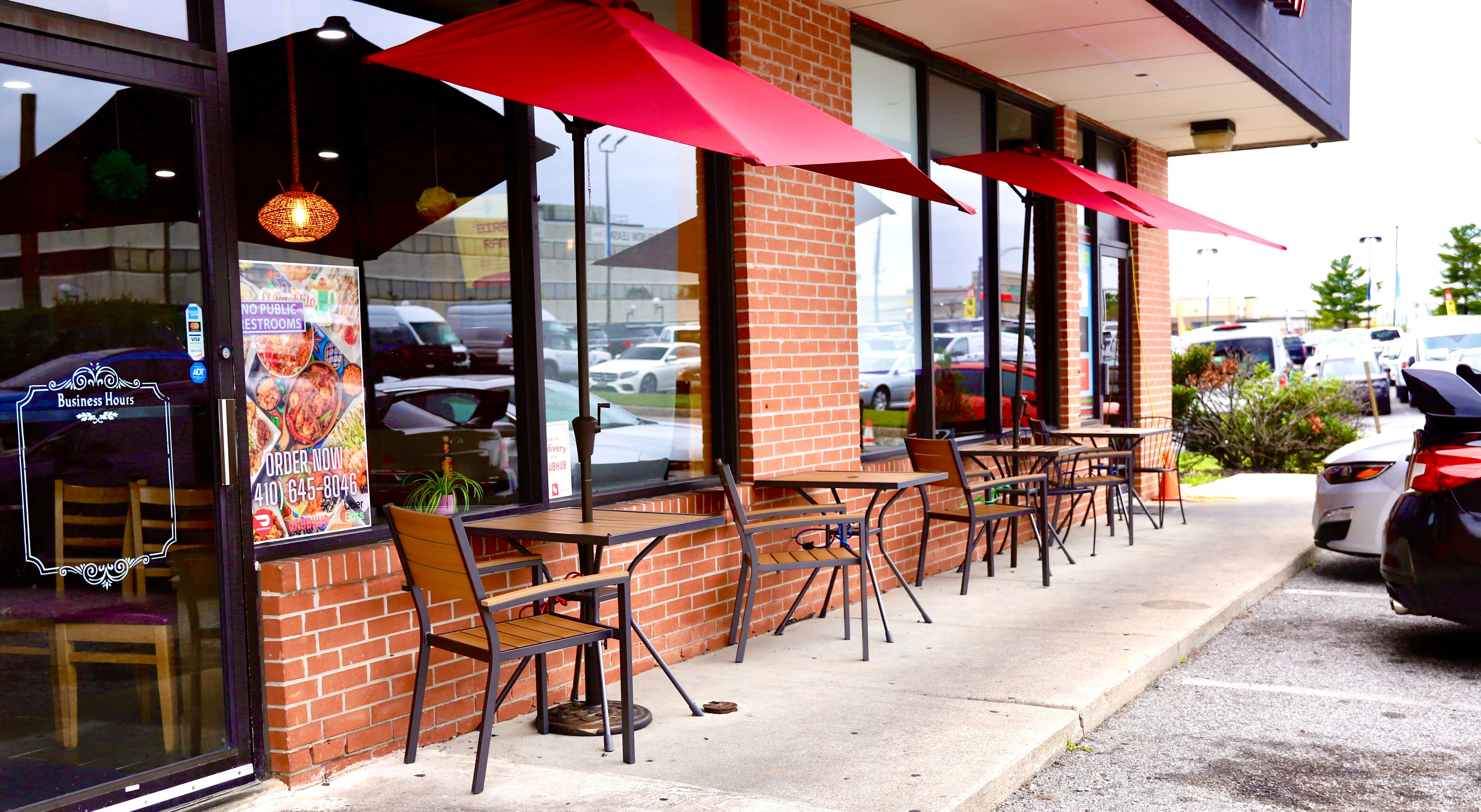 Outdoor dining area with red umbrellas and brick facade