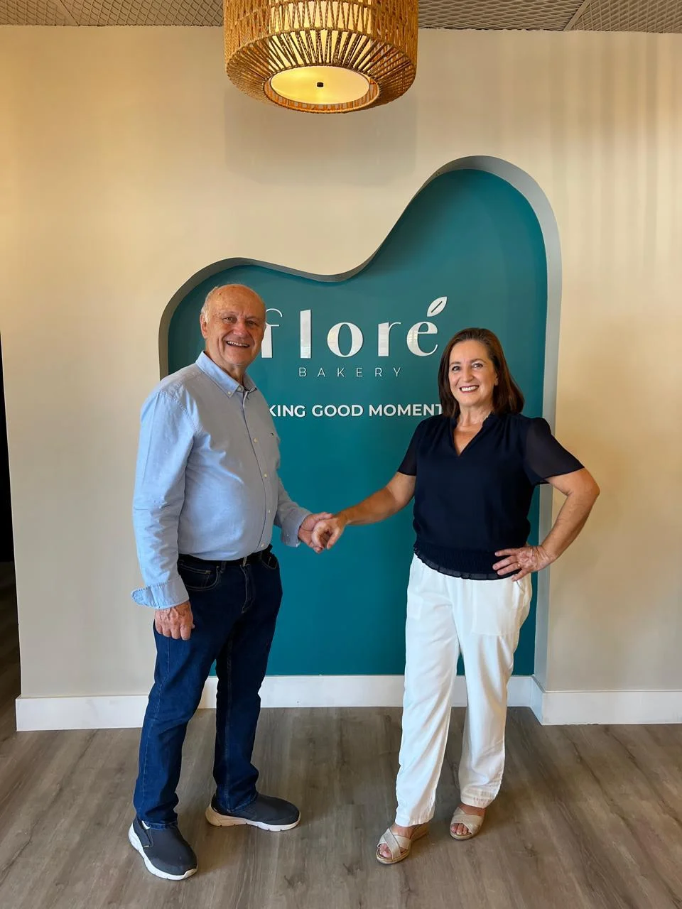 Two people shaking hands in front of Flore Bakery sign