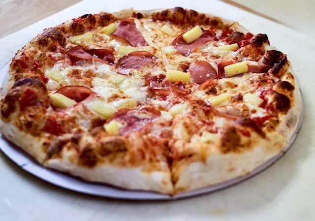 A delicious pizza topped with ham and pineapple slices.