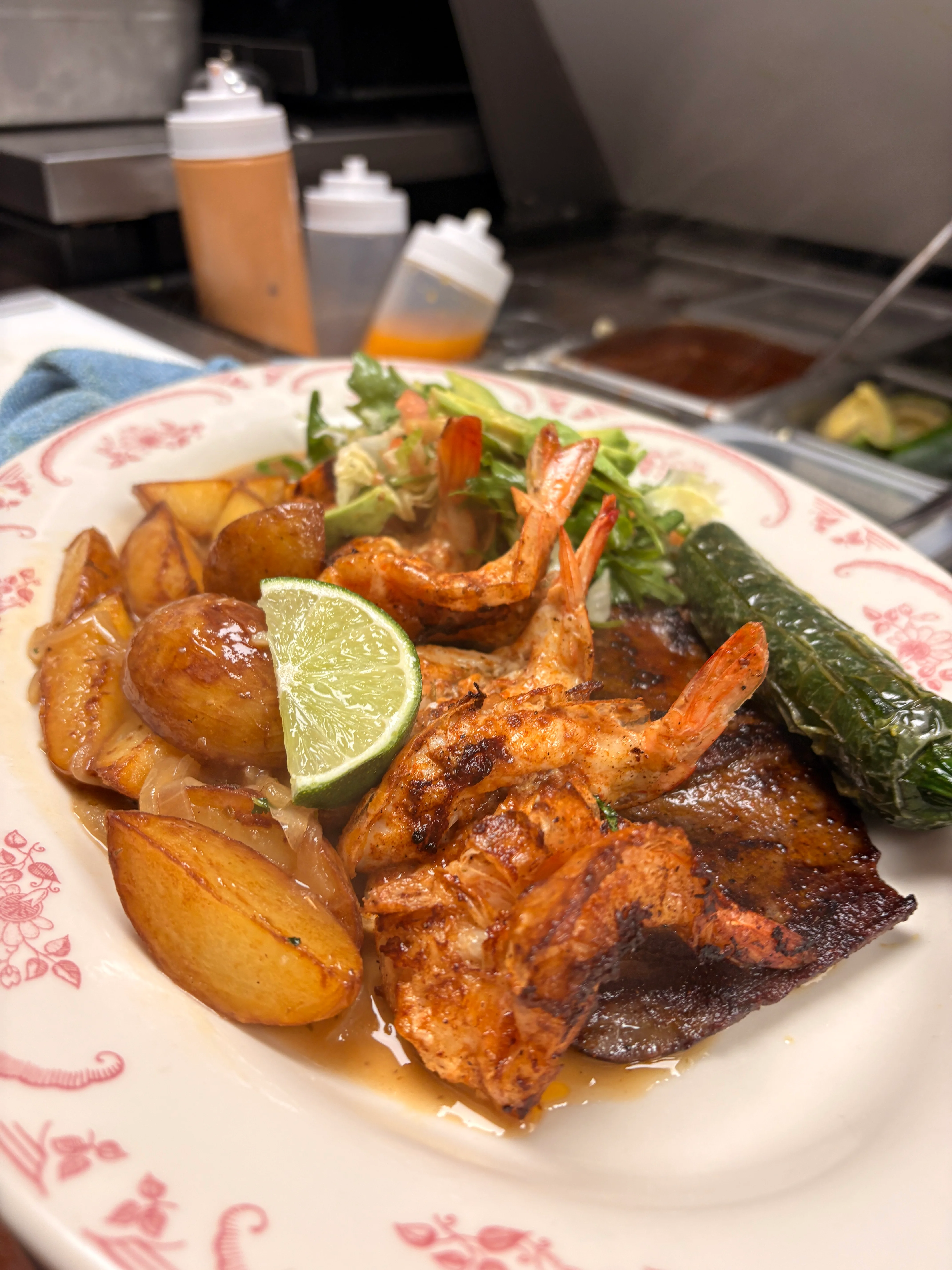 A delicious plate featuring grilled shrimp, potatoes, a slice of lime, and a green pepper, garnished with lettuce.