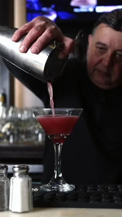 A bartender skillfully pouring a pink cocktail from a shaker into a martini glass.