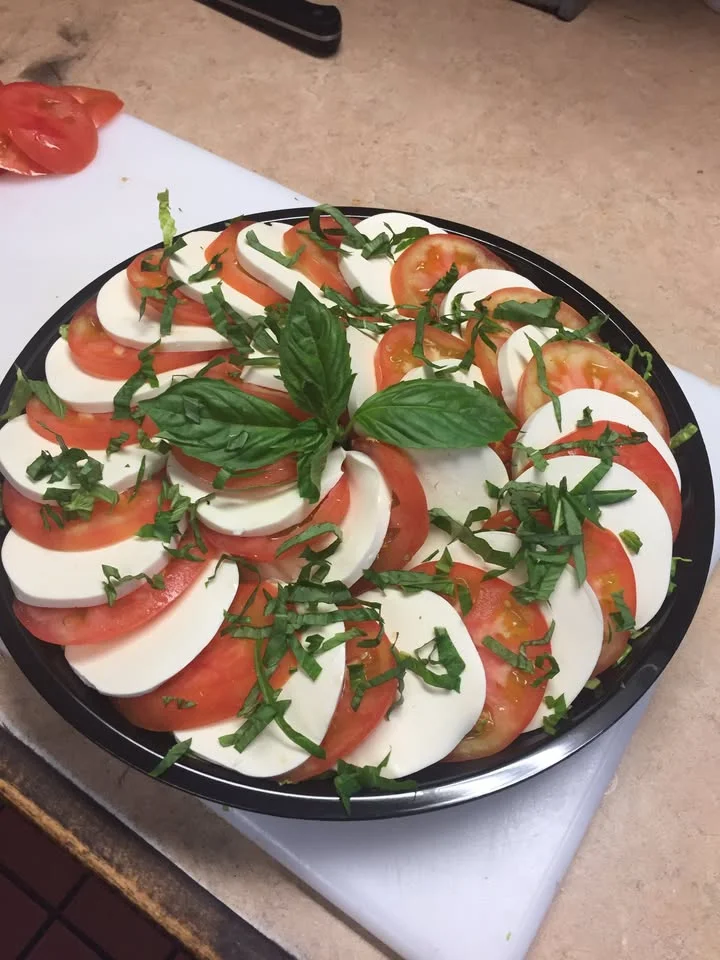 A circular arrangement of sliced tomatoes and mozzarella cheese, topped with fresh basil, creating a vibrant and appetizing dish.