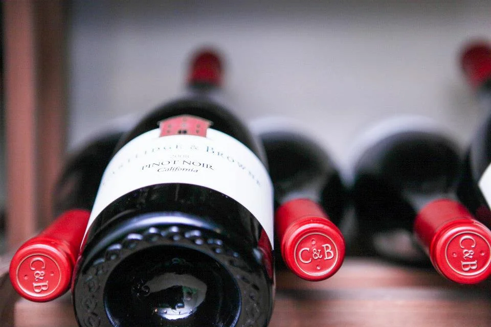 A close-up of several bottles of red wine neatly arranged on a shelf, showcasing the caps and their labels.