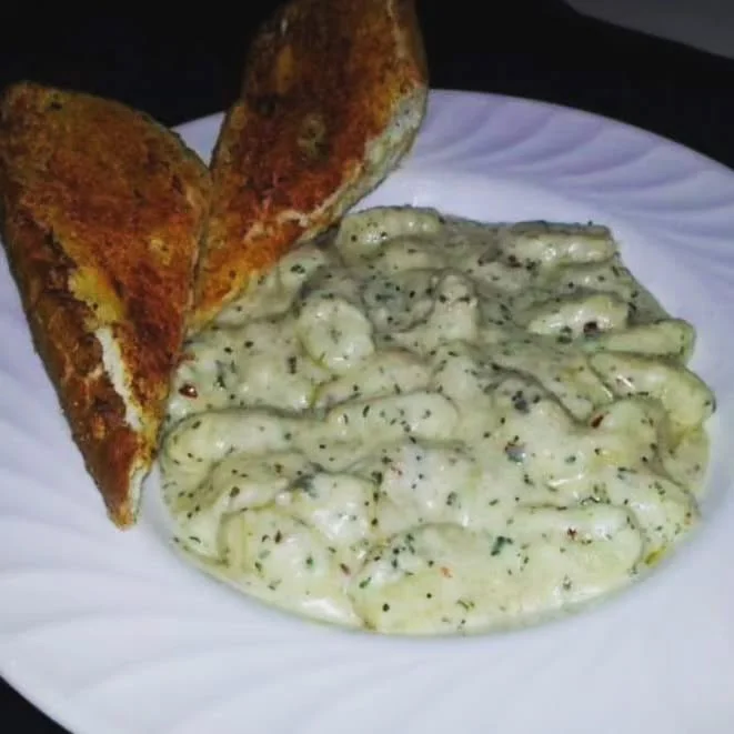 Creamy gnocchi with garlic bread on a white plate