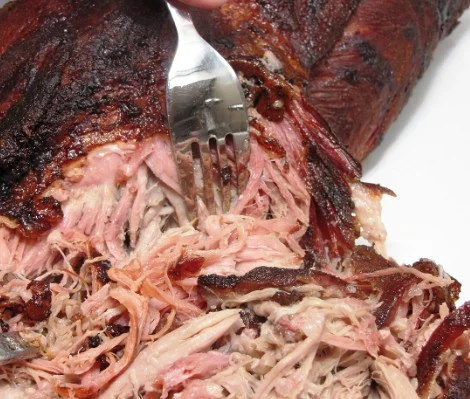 Close-up of pulled pork with a fork, showcasing tender meat texture.