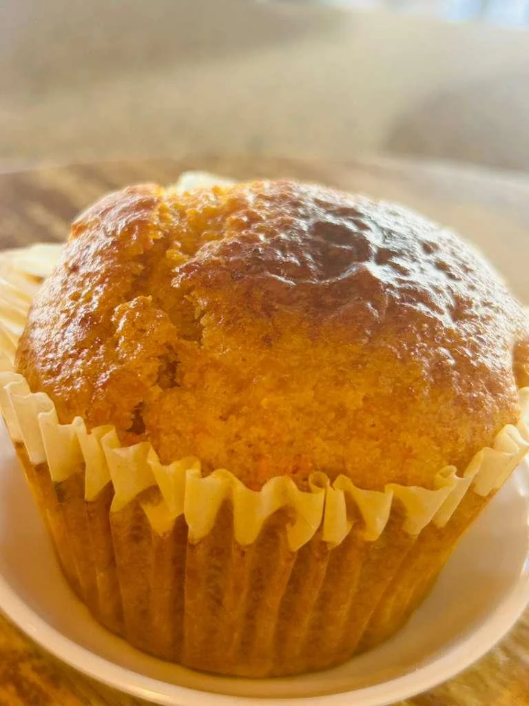 A freshly baked muffin sitting in its wrapper, showcasing a golden-brown top.