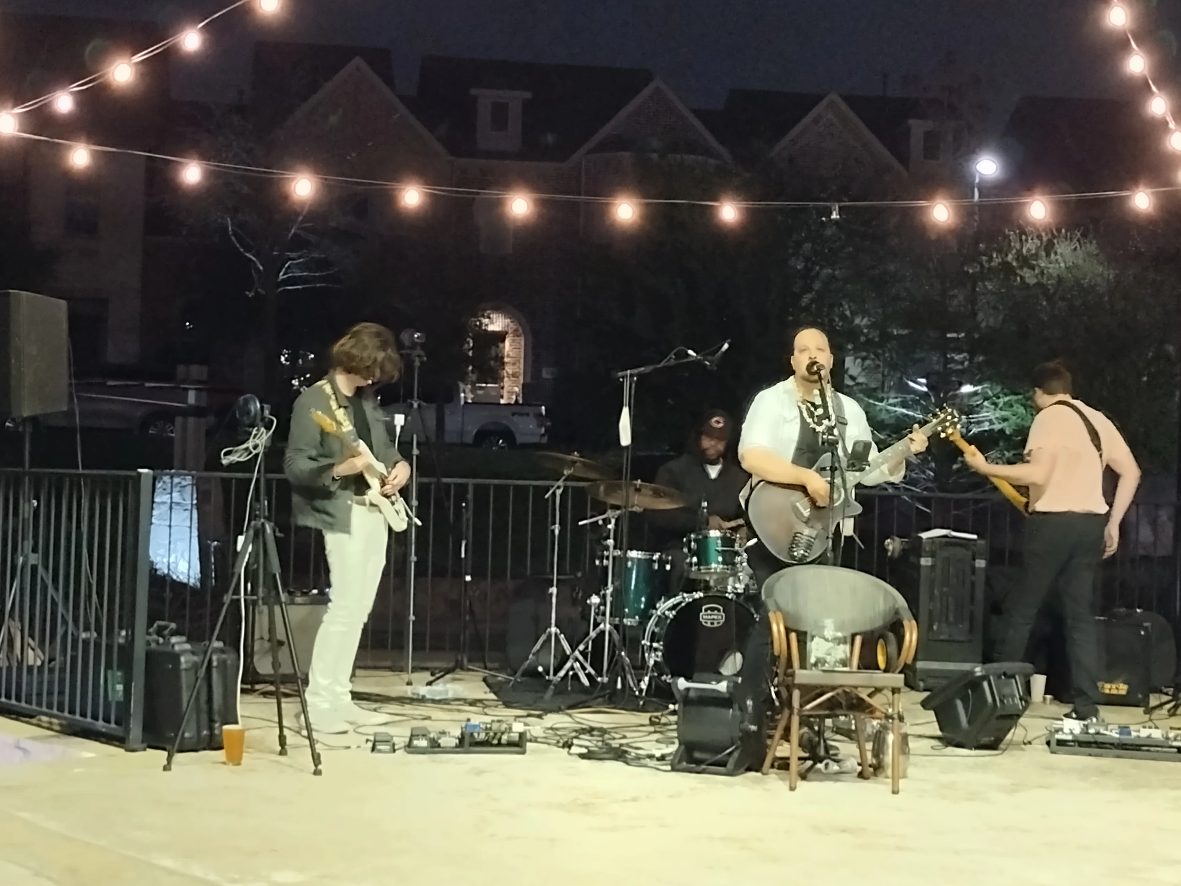 Live band performing at an outdoor venue with string lights