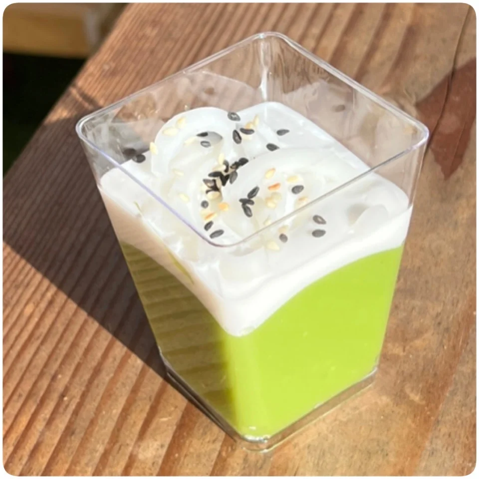 A green dessert with whipped cream and sesame seeds in a clear cup.