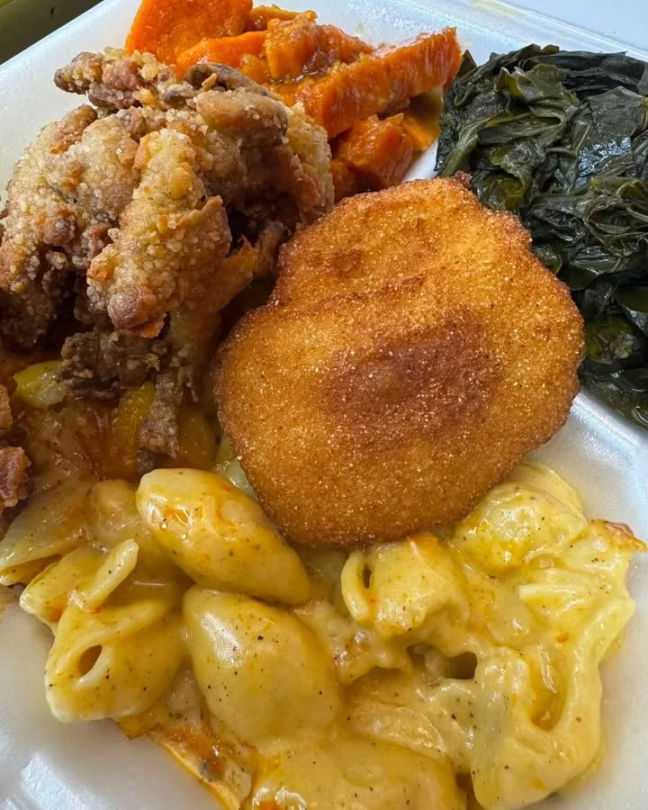 A plate featuring a hearty meal with fried chicken, macaroni and cheese, collard greens, and sweet potatoes.