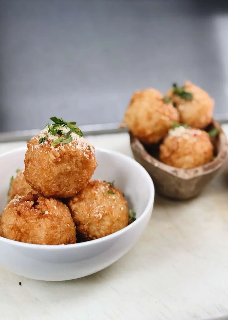 Fried dough balls garnished with herbs in a white bowl.