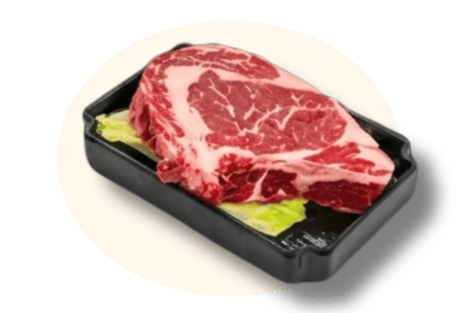 A marbled steak on a bed of lettuce in a black tray.