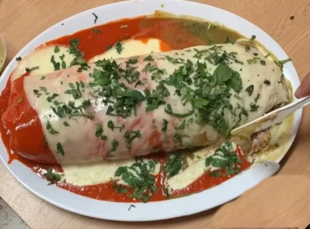 Giant burrito smothered in sauce and cheese, topped with fresh cilantro