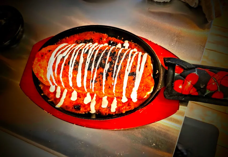 A vibrant red wet burrito topped with sauce and garnished.