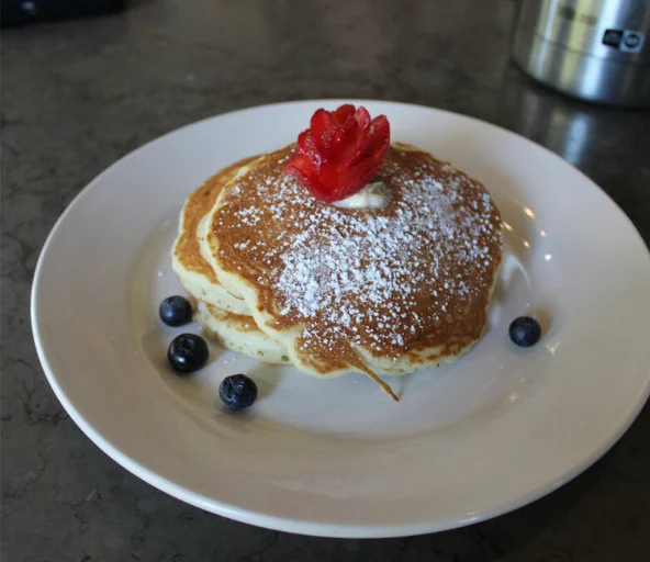 Fluffy American pancakes topped with a strawberry and powdered sugar