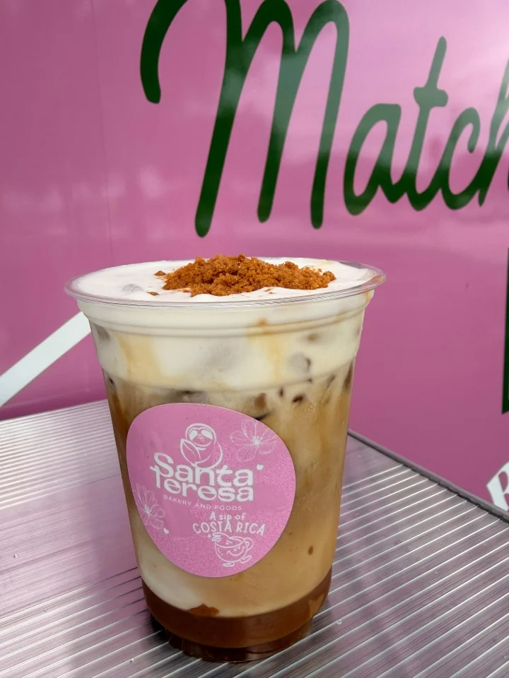 A refreshing iced drink layered with cream and topped with a sprinkle of brown sugar, served in a clear cup.
