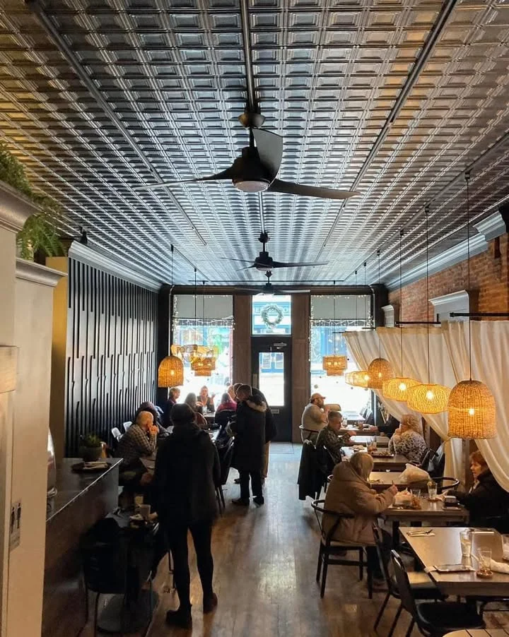 An indoor dining area featuring a decorative ceiling, wooden flooring, and several tables with patrons enjoying their meals.