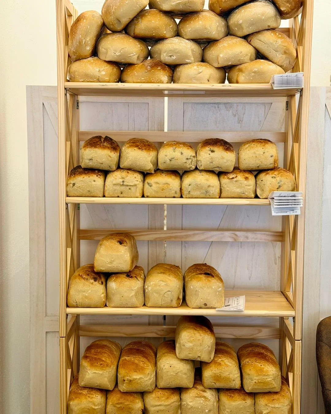 A wooden shelf stacked with neatly arranged small loaves of freshly baked bread, showcasing a variety of textures.