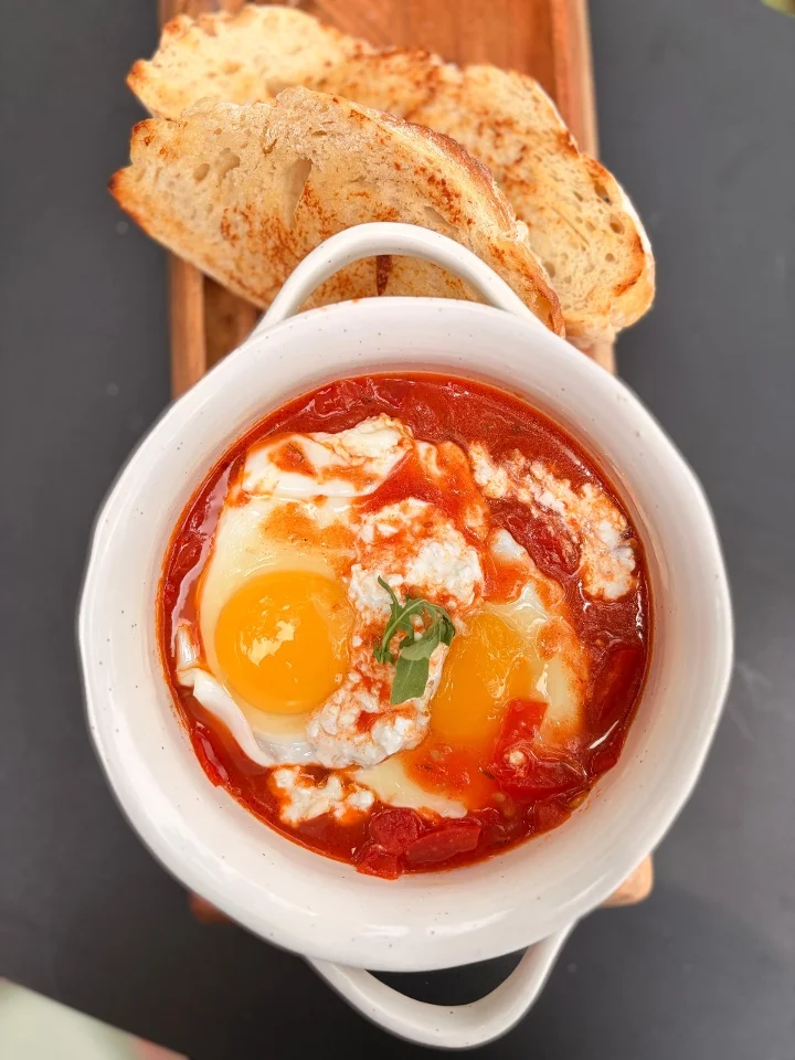 A flavorful dish featuring poached eggs in a spicy tomato sauce, served alongside toasted bread.