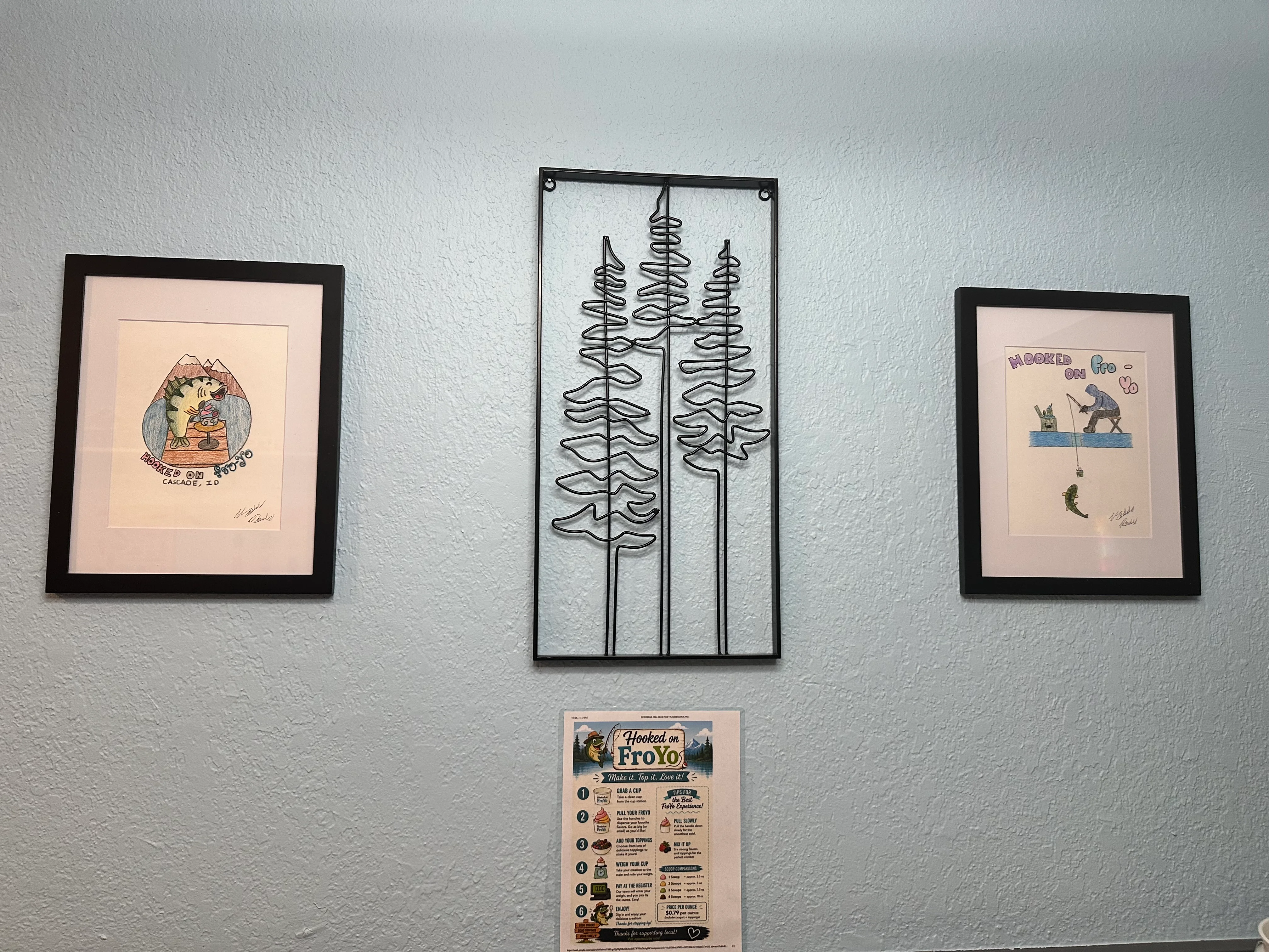 A decorative wall featuring framed art prints of whimsical animals and a wire sculpture of trees, along with a menu for a frozen yogurt shop.