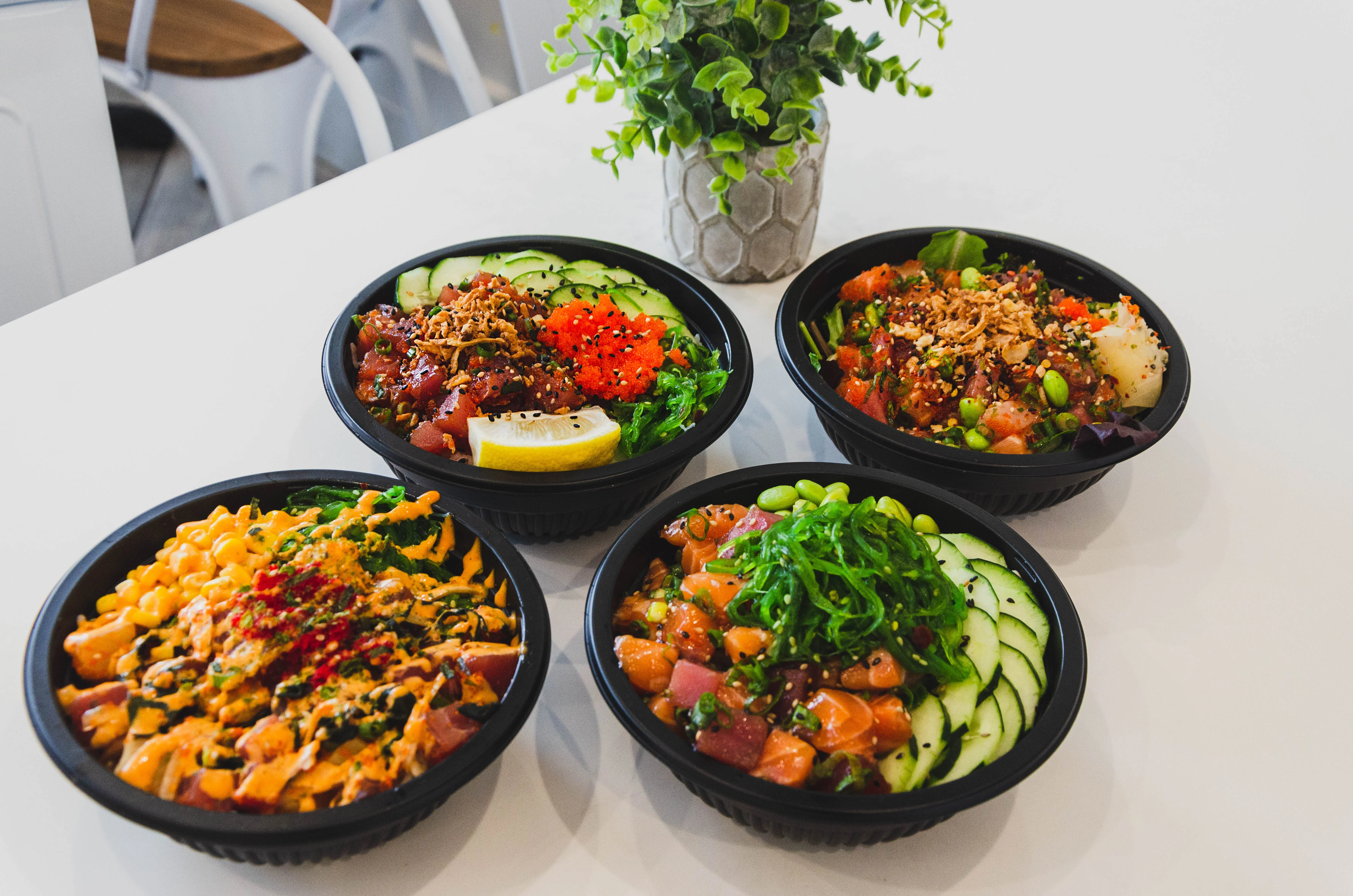 Four bowls filled with various ingredients, including fish, vegetables, and toppings, presented on a white table.