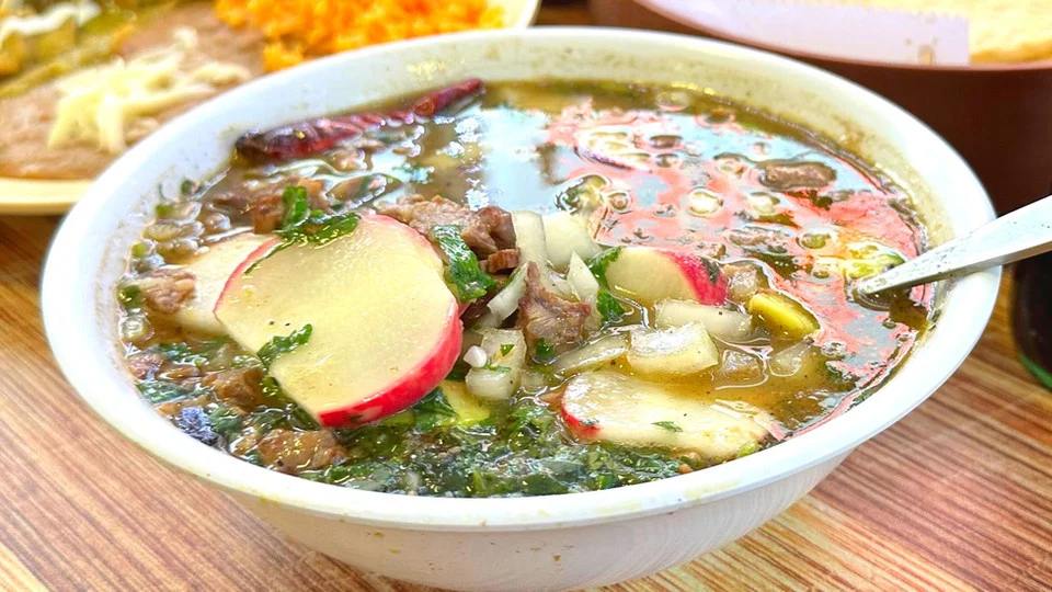 Bowl of Mexican pozole with fresh herbs and radishes